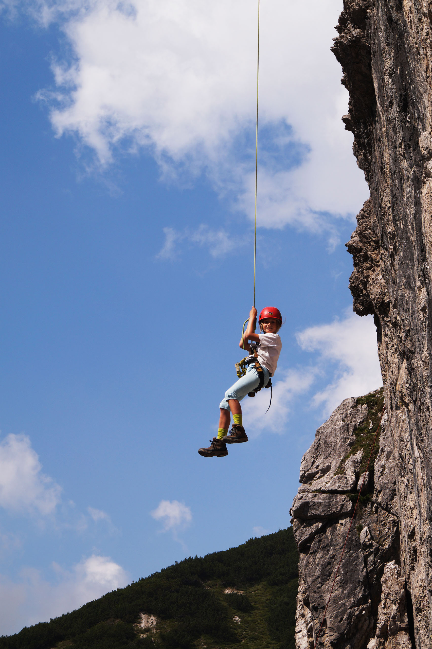 Mädchen strahlt in die Kamera, während es gerade vom Top abgeseilt wird